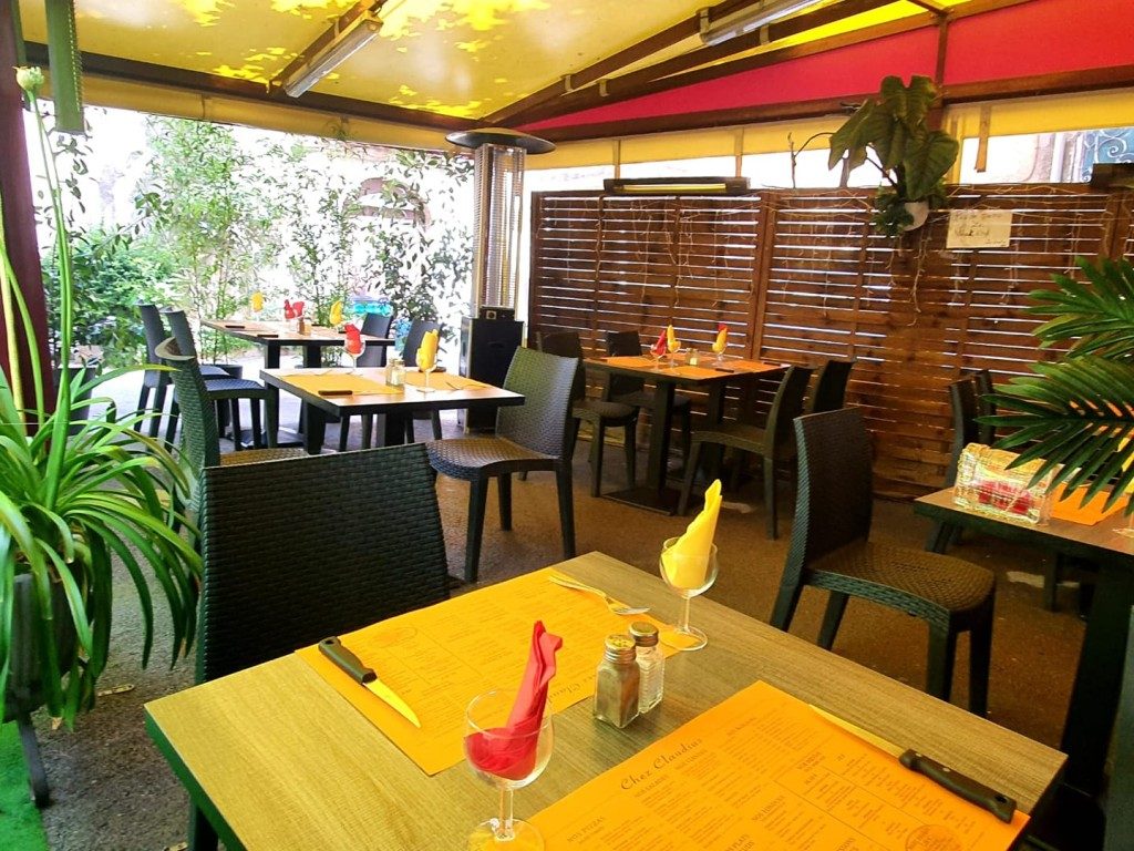La terrasse couverte : tables jaunes, banquettes et plantes vertes